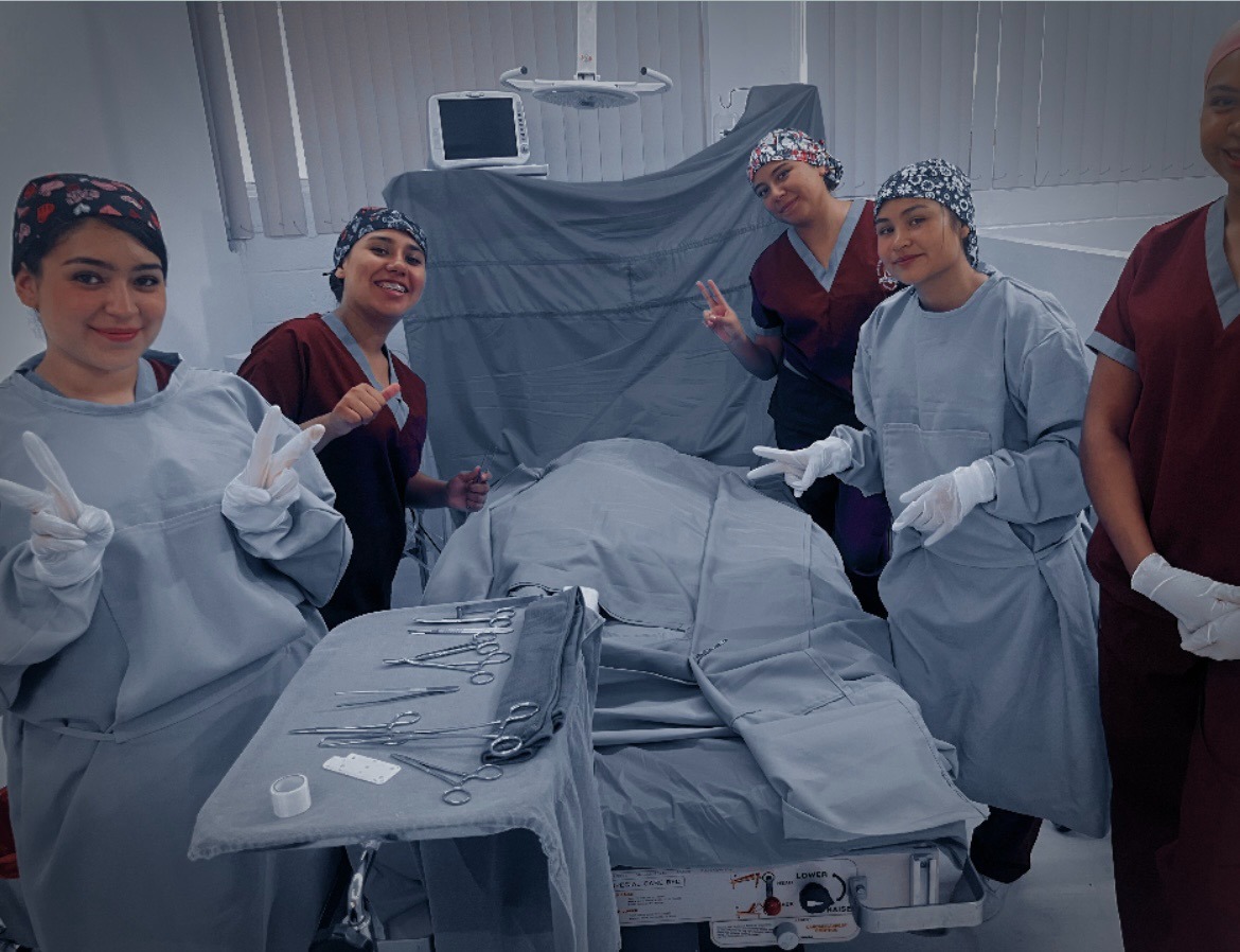Estudiantes de enfermería con uniforme quirúrgico en una sala de práctica clínica.