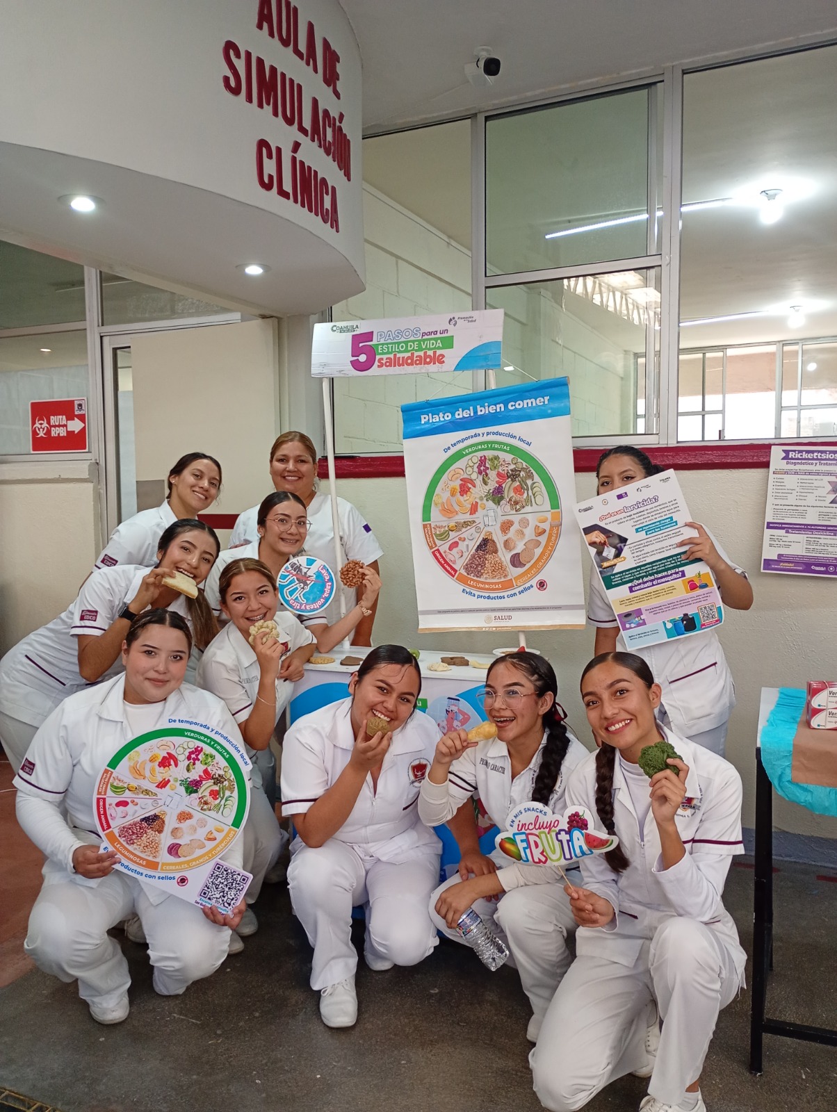 Estudiantes en uniforme blanco en el aula de simulación clínica con material educativo.