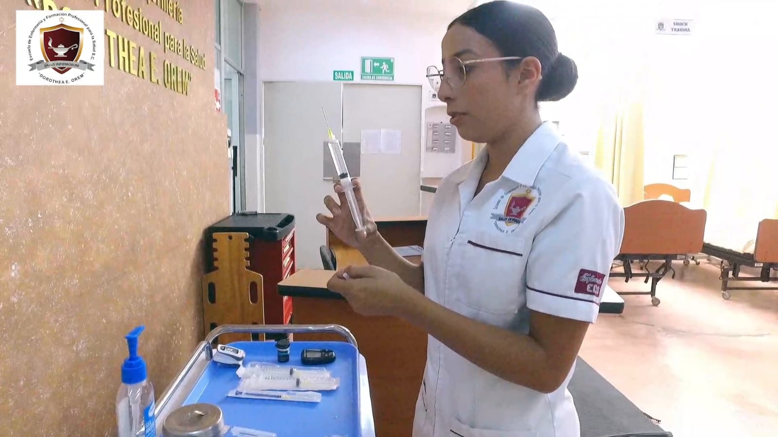 Estudiante de enfermería con uniforme blanco preparando una inyección durante su práctica.